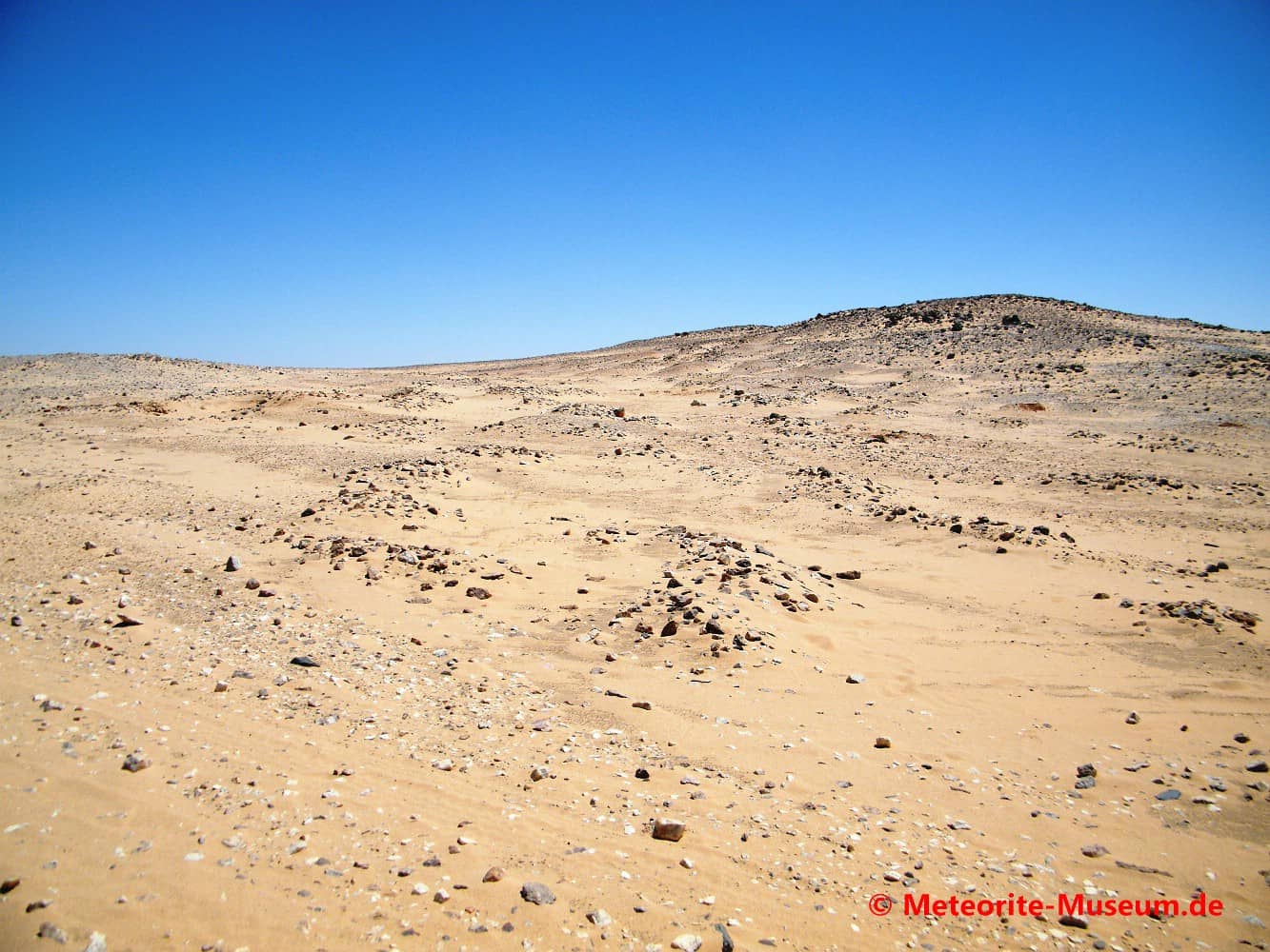 Die nubische Wüste mit Steinfelder, Hügel und tief blauem Himmel nahe der Almahata Sitta Meteoriten-Fundstelle