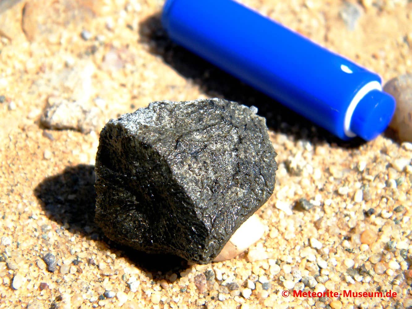 Almahata Sitta Meteorit Bruchstück mit schwarz-grüner Schmelzkruste und GPS-Gerät